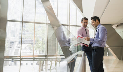 Corporate businessmen discussing paperwork in modern lobby - CAIF06788