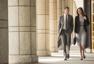 Corporate businessman and businesswoman walking and talking in cloister - CAIF06795