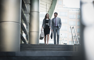 Corporate businessman and businesswoman descending stairs outdoors - CAIF06816