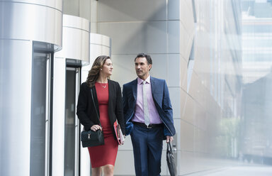 Corporate businessman and businesswoman walking and talking outside building - CAIF06817