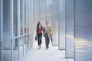 Corporate businessman and businesswoman walking along modern building - CAIF06824