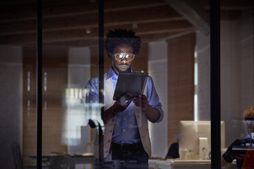 Designprofi, der nachts in einem dunklen Büro mit einem digitalen Tablet arbeitet - CAIF06875