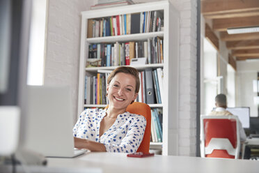 Porträt einer lächelnden, selbstbewussten Geschäftsfrau, die im Büro am Laptop arbeitet - CAIF06887