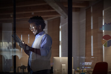 Smiling businesswoman working late, using digital tablet in dark office at night - CAIF06896