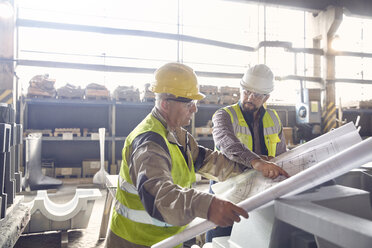 Steelworker and engineer reviewing blueprints in steel mill - CAIF06913