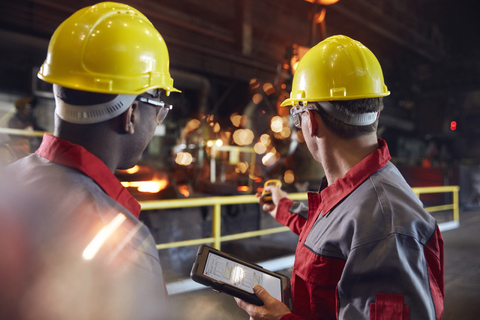 Aufsichtsperson und Stahlarbeiter mit digitalem Tablet in einem Stahlwerk, lizenzfreies Stockfoto