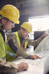 Engineer and steelworker discussing blueprints in steel mill - CAIF06939