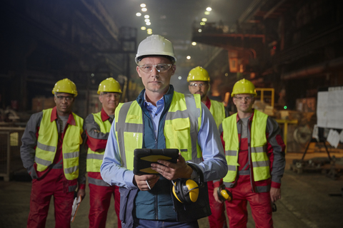 Porträt eines selbstbewussten Aufsehers und von Stahlarbeitern in einem Stahlwerk, lizenzfreies Stockfoto