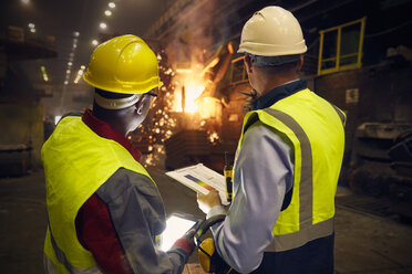 Stahlarbeiter mit digitalem Tablet und Klemmbrett im Gespräch im Stahlwerk - CAIF06949