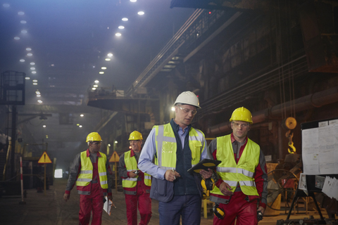 Aufsichtsperson und Stahlarbeiter gehen und sprechen in einem Stahlwerk, lizenzfreies Stockfoto