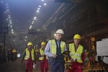 Aufsichtsperson und Stahlarbeiter gehen und sprechen in einem Stahlwerk - CAIF06950