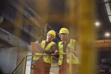 Stahlarbeiter mit Klemmbrett im Gespräch auf einer Plattform im Stahlwerk - CAIF06955