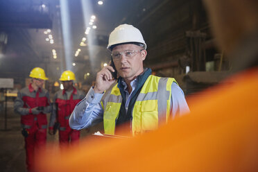Aufsichtsperson im Stahlwerk, die mit einem Smartphone telefoniert - CAIF06958
