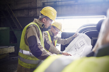 Engineer and steelworker examining blueprints in steel mill - CAIF06975