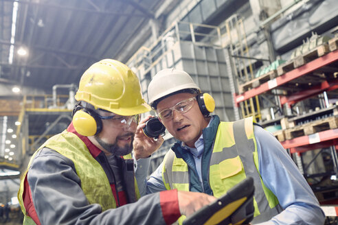 Steelworkers wearing ear protectors using digital tablet in steel mill - CAIF06979