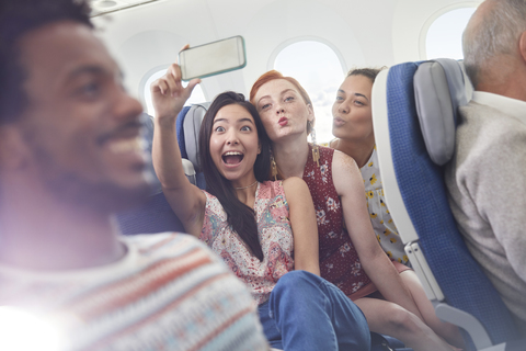 Verspielte junge Freunde mit Fotohandy machen ein Selfie im Flugzeug, lizenzfreies Stockfoto