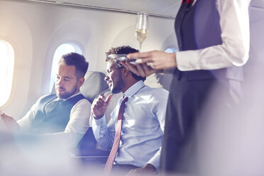 Flugbegleiter serviert Champagner an Geschäftsleute in der ersten Klasse im Flugzeug - CAIF06990