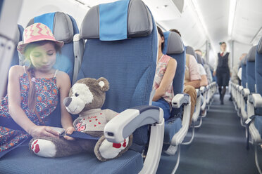 Girl fastening seat belt on stuffed animal on airplane - CAIF06994