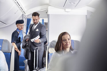 Flight attendant helping businessman with boarding pass on airplane - CAIF06995