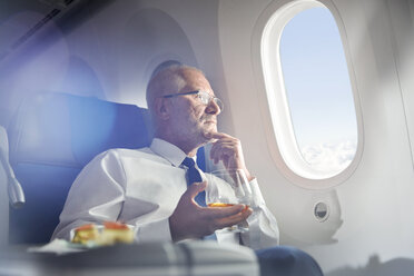 Älterer Geschäftsmann trinkt Whiskey in der ersten Klasse und schaut aus dem Flugzeugfenster - CAIF07001