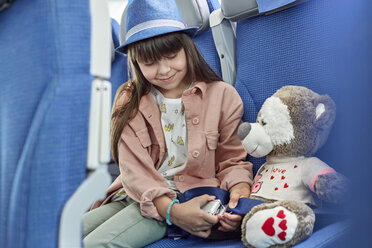 Girl fastening seat belt on stuffed animal on airplane - CAIF07006