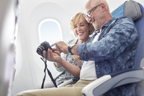 Älteres Paar betrachtet Fotos auf einer Digitalkamera im Flugzeug, lizenzfreies Stockfoto