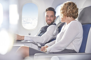 Lächelnder Geschäftsmann und Geschäftsfrau im Gespräch im Flugzeug - CAIF07011