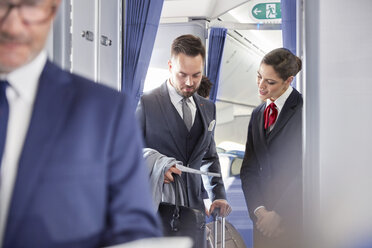 Flight attendant helping businessman with boarding pass on airplane - CAIF07019