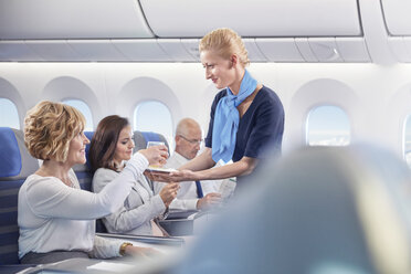 Flugbegleiter serviert einer Frau im Flugzeug ein Getränk - CAIF07024