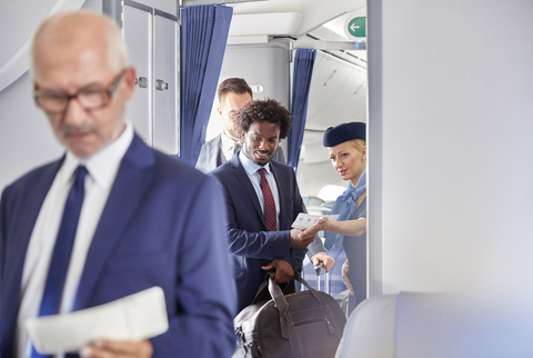 Flugbegleiter hilft Geschäftsmann mit Bordkarte im Flugzeug, lizenzfreies Stockfoto