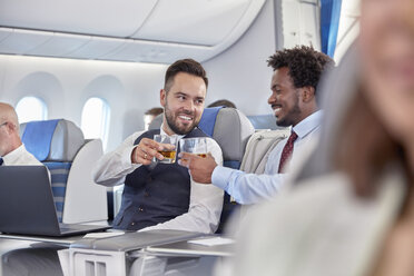 Geschäftsleute stoßen in der ersten Klasse eines Flugzeugs mit Whiskeygläsern an - CAIF07036