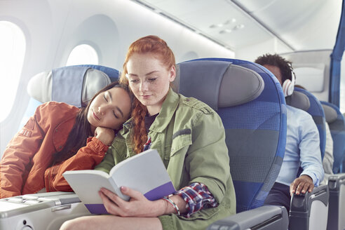 Zärtliches junges lesbisches Paar, das im Flugzeug schläft und liest - CAIF07041