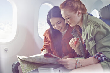 Young women friends looking at map on airplane - CAIF07045