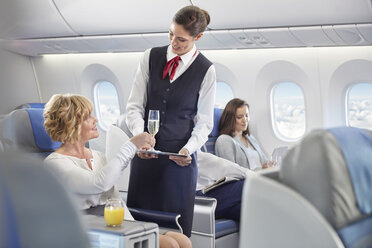 Flugbegleiter serviert Frau in der ersten Klasse Champagner im Flugzeug - CAIF07048