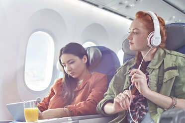 Young women friends with headphones and digital tablet on airplane - CAIF07050