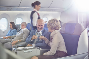 Reifes Paar stößt mit Champagnergläsern in der ersten Klasse eines Flugzeugs an - CAIF07052