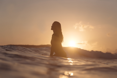 Indonesien, Lombok, weibliche Surferin auf Surfbrett sitzend bei Sonnenuntergang, lizenzfreies Stockfoto