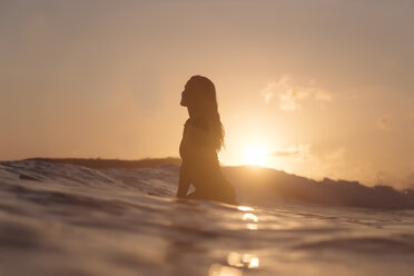 Indonesien, Lombok, weibliche Surferin auf Surfbrett sitzend bei Sonnenuntergang - KNTF01083