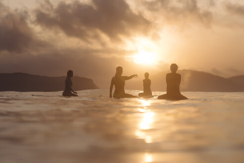 Indonesien, Lombok, Gruppe von Surfern auf Surfbrettern sitzend bei Sonnenuntergang - KNTF01084