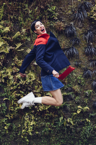 Porträt einer modischen jungen Frau, die vor der Living Wall in die Luft springt, lizenzfreies Stockfoto