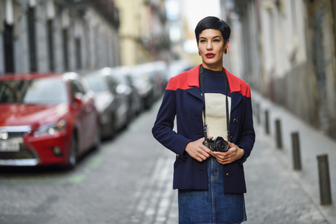 Portrait of fashionable young woman with camera on the street stock photo