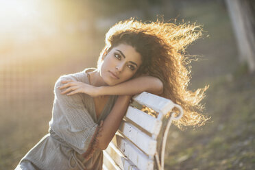 Porträt einer jungen Frau, die sich auf einer Bank in einem Park bei Sonnenuntergang ausruht - JSMF00101