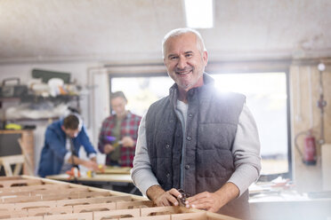 Porträt lächelnder männlicher Schreiner bei der Arbeit an einem Holzboot in einer Werkstatt - CAIF07070