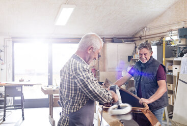 Male carpenters buffing wood kayak with sander in workshop - CAIF07075