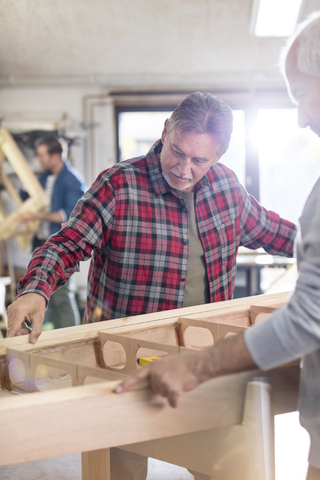 Männliche Zimmerleute prüfen ein Holzboot in der Werkstatt, lizenzfreies Stockfoto