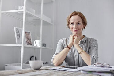 Porträt einer lächelnden, selbstbewussten Geschäftsfrau, die ein digitales Tablet benutzt und im Büro Tee trinkt - CAIF07089