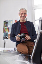 Portrait smiling, confident male photographer with digital camera in office - CAIF07093