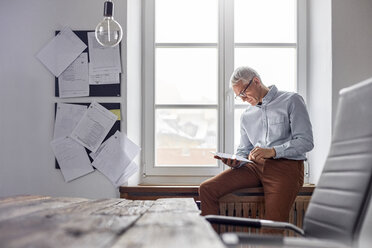 Businessman using digital tablet in office window - CAIF07098