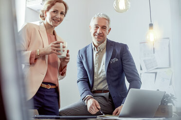 Portrait lächelnde, zuversichtliche Geschäftsleute, die Kaffee trinken und am Laptop im Büro arbeiten - CAIF07100