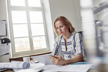 Female architect using digital tablet in office with blueprints - CAIF07117